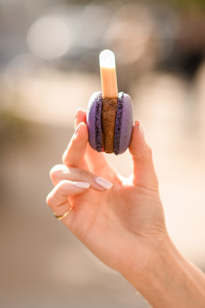 close-up view of female hand holding delicious purple macaron on blurred backgroundの写真素材
