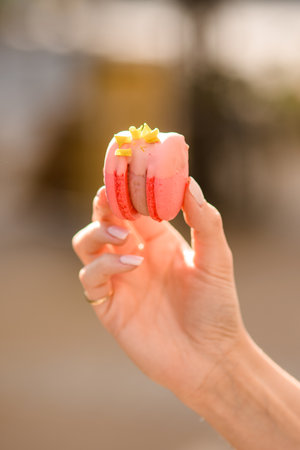 close-up view of female hand holds delicious bright pink macaron on blurred backgroundの写真素材
