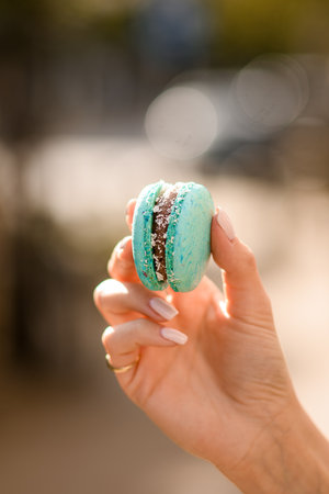 close-up of female hand holds delicious turquoise macaron on blurred backgroundの写真素材