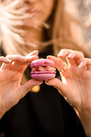 Selective focus on delicious pink macaron in female hands on blurred backgroundの写真素材