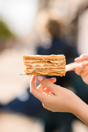 Close-up view on female hand gently holding slice of sweet honey cake on a metal cake spatulaの写真素材