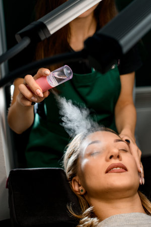 great close-up view of female client and beautician moisturizes her face with steam from portable...