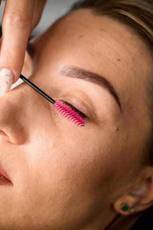 close-up view of closed eye of woman and beautician combing the eyelashes with a nylon eyelash brush