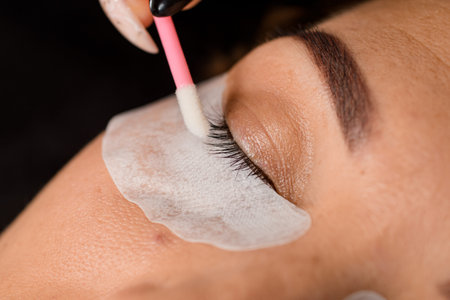 close-up view of closed eye of female and beautician spreads eyelashes with cotton swab