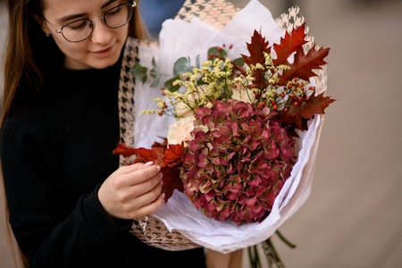 Young woman looks on a big and beautiful autumn style bouquet of fresh flovers and oak leavesの写真素材