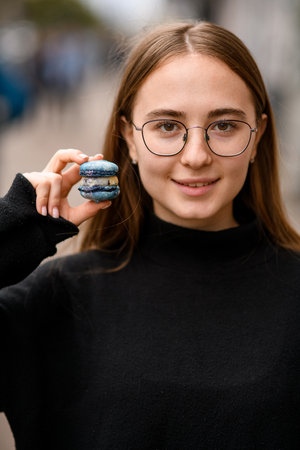 beautiful brown eyed girl in glasses holds in her hand blue french macaroonの写真素材