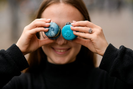 Beautiful girl wear in black keeps two sweet french macaroons on eyesの写真素材