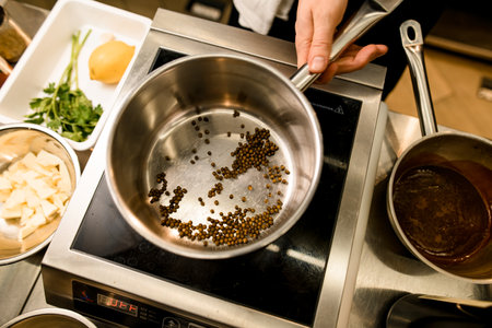 Mans hand holding steel stewpan standing on kitchen scales. Chief cooking spices in stewpan.の写真素材