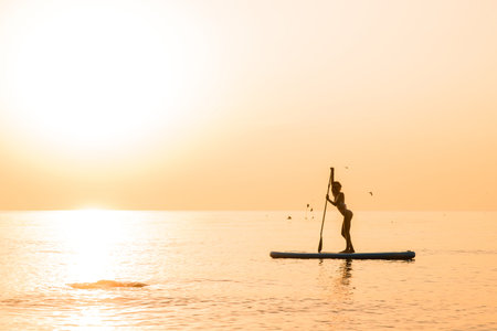 Stunning silhouette of beautiful girl floating on on the surf board