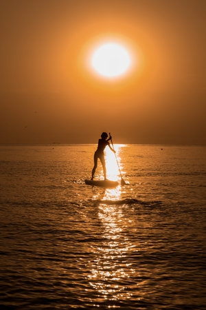 Silhouette of beautiful girl floating on on the surf board over the sea