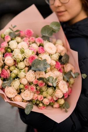 Close-up of beautiful bouquet of colorful roses with eucalyptus branches in wrapping paper in womans handsの写真素材
