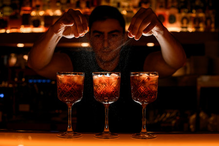 Barman sprinkle glasses with alcoholic cocktails with piece of orange citrus zestの写真素材
