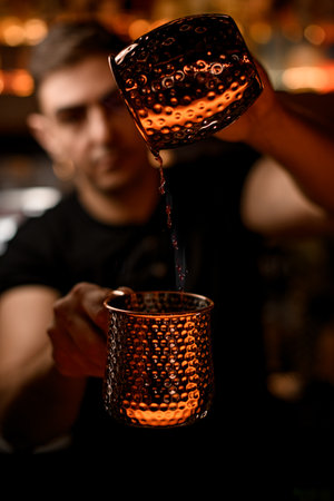 Handsome male bartender pouring drops of alcoholic drink from one steel cup to anotherの写真素材
