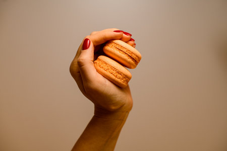Girls hand with bright red manicure hold bright yellow halves of macarons on light backgroundの写真素材