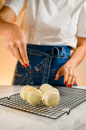 Woman chef with bright red manicure sprinkles freshly made macaroons with chopped peanuts and pistachiosの写真素材