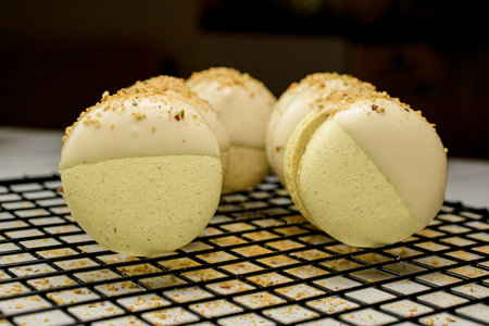 Fresh tasty pistachio macarons with sweet ganache decorated with white chocolate, chopped peanuts...