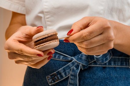 Woman confectioners hands connecting two shells of macarons and puts wooden ice stick between themの写真素材