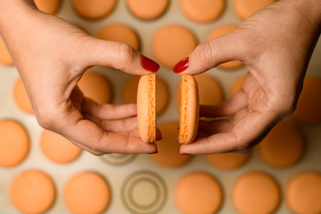 Close-up view of females hands connect together two halves of macaroons. Selective focus.の写真素材