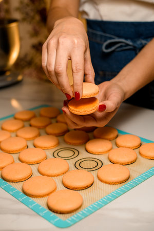Woman chefs hands hold and connect together two fresh baked crispy and sweet halves of macaroons.の写真素材