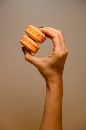 Womans hand with bright red manicure hold bright yellow halves of macarons on light backgroundの写真素材