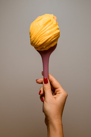 Confectioners hand holds mango or apricot sweet ganache on pink silicone spatula for covering and decorating cakes, macaronsの写真素材