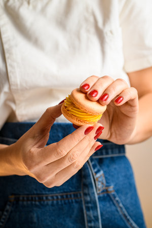 Confectioners hands with red manicure connecting two halves of macarons, decorated with ganacheの写真素材
