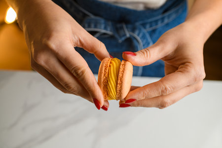Top view of female confectioners hands with red manicure connecting two halves of macaronsの写真素材