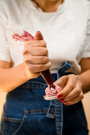 Girl squeezing fruit jam from confectionery bag into ganache cream on macarons halves, close up view