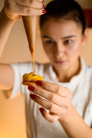 Chef woman squeezing tasty cream filling from confectionery bag to fresh macaron halfの写真素材