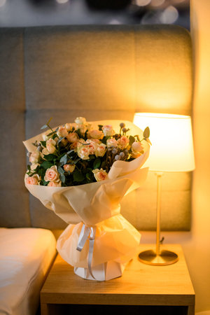 Large beautiful bouquet of roses and twigs of green on nightstand in modern bedroomの写真素材