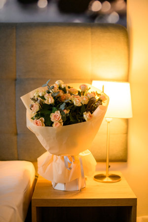 Beautiful bouquet of creamy roses and twigs of green on nightstand in modern bedroomの写真素材