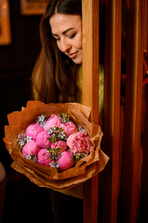 Young beautiful woman posing with bouquet of peonies near wooden doorsの写真素材