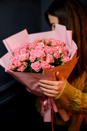 Young darkhair woman florist holding in hands large bouquet of fresh pink rosesの写真素材