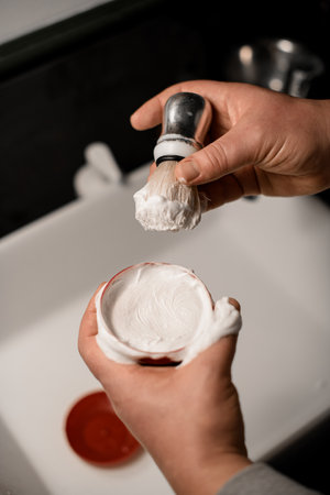 Close up photo of barbers hands holding bowl with shaving cream and steel shaving brushの写真素材