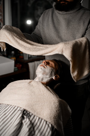 Man barber holding towel above male clients face in barber shop interiorの写真素材