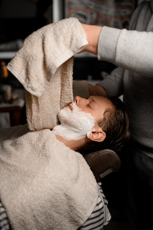Professional barber holding towel above male clients face in barber shop interiorの写真素材