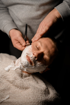 Barber shaving client with vintage straight razor. Classic shave by stainless steel straight edge razorの写真素材