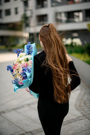 Rear wiew on girl in black outfit with bouquet of flowers outdoors. Young woman holding bouquet og colorful fresh flowers.の写真素材