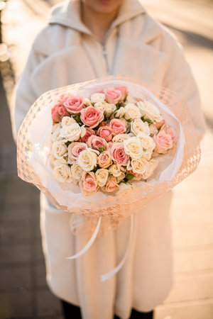 Bunch of fresh small roses in pink and milk colors formed in bouquet with wrapping paper and white silk ribbon in womans handsの写真素材