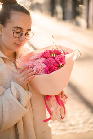 Attractive girl holding beautiful bouquet of fresh pink roses and carnations in wrapping paper with flower shopの写真素材