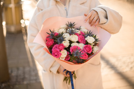 Selective focus on flowers bouquet with creamy and pink roses and thistles formed in wrapping paper with blue satin ribbon in womans handsの写真素材