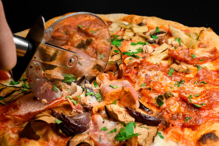 Womans hand cutting fresh hot pizza with roller knife on wooden boardの写真素材