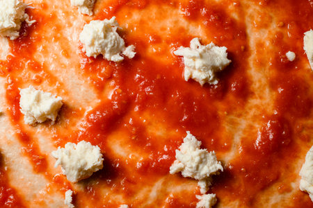 Top view of raw dough for pizza preparation with ingredient: tomato sauce, mozzarella pieces