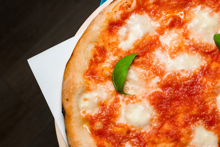 Close up view of fresh cooked homemade pizza on wooden serving board on black background.