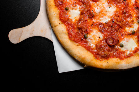 Sliced freshly baked mexican pizza with pepperoni, cheese, green peas and red chili peppers on wooden serving boardの写真素材