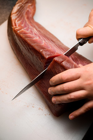 View from above on chef using Japanese knife and cutting fresh and raw big tuna fillet at restaraunt...