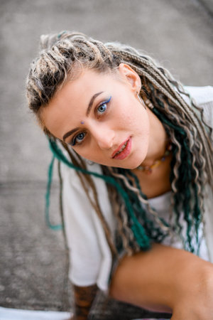 Beautiful blonde woman with colorful braids in hair in white clothes posing on blured background