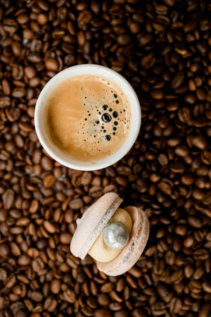 White cup with coffee and macaroon on top of fresh roasted coffee beans, top viewの写真素材