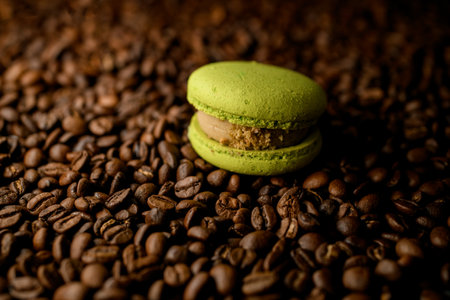 Selective focus of tasty sweet french dessert macaron with lime taste and fruit filling on roasted coffee beans backgroundの写真素材