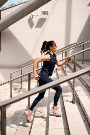 Young attractive woman in sportswear doing a warm-up on stairs before training outdoor in summer...